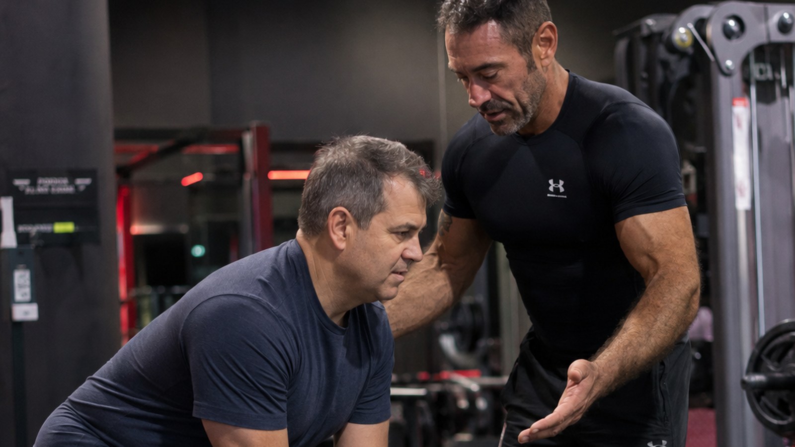 A strong, lean man in his forties pressing dumbbells in a dark, dramatically lit gym